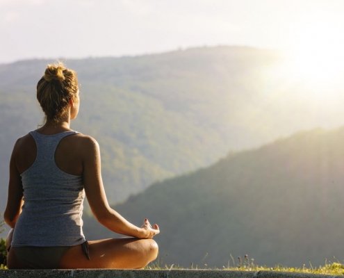 Junge Frau meditiert vor wundervoller Naturkulisse, Foto zum Blogeintrag über Yoga bei JOYA International Massageprodukte